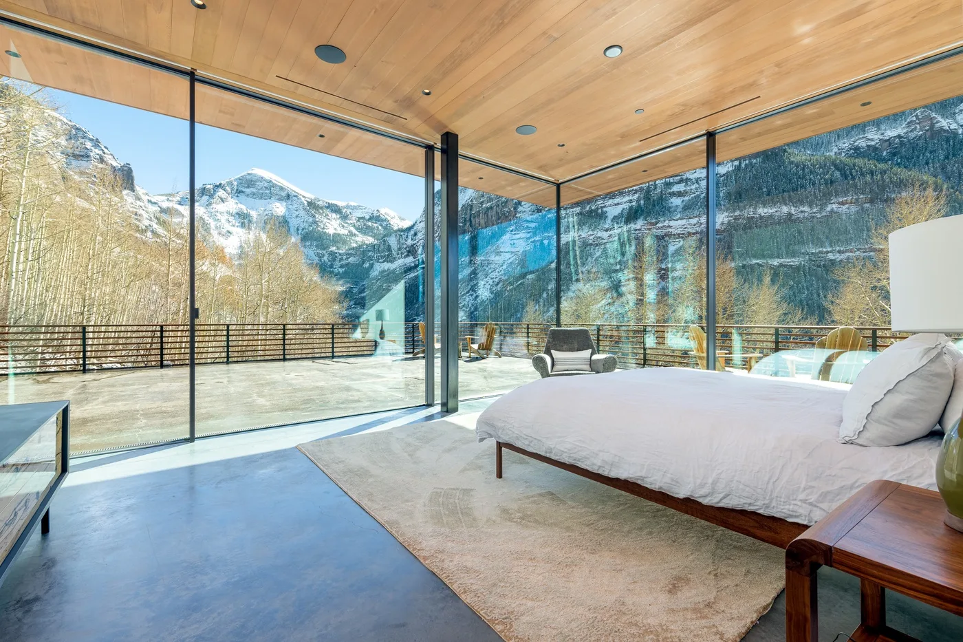 Un dormitorio con una cama junto a ventanales con vistas a un paisaje montañoso nevado.