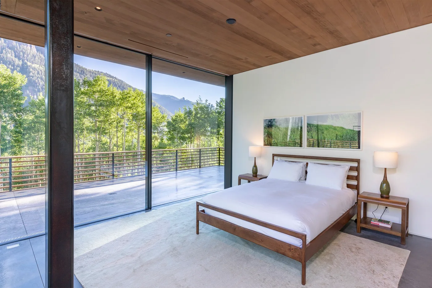 Un dormitorio con una cama junto a ventanales con vistas a árboles y montañas.