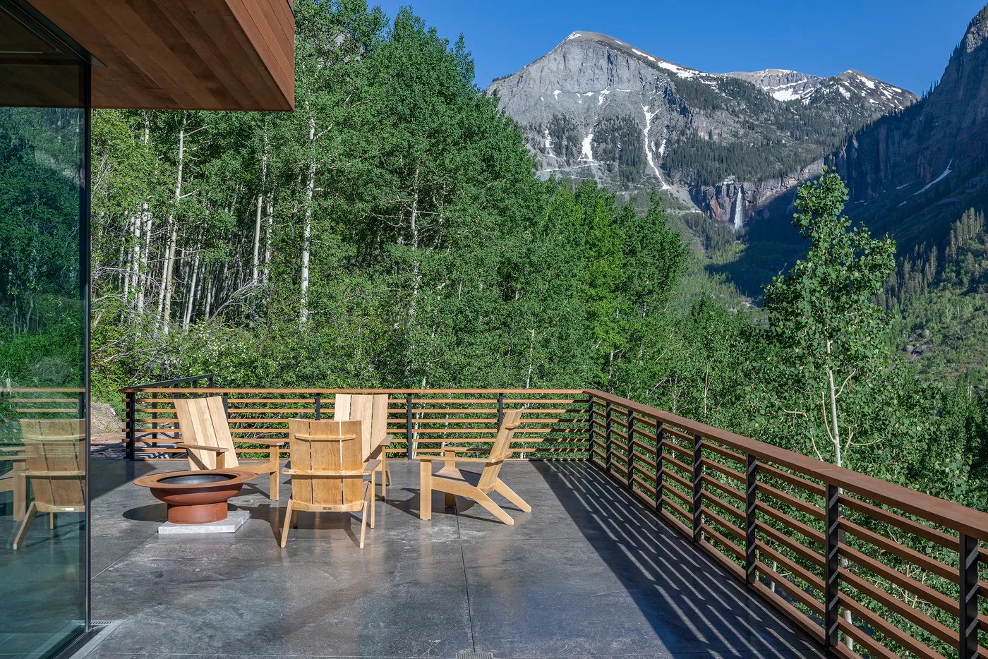Una terraza exterior con asientos ofrece vistas a un valle montañoso boscoso.