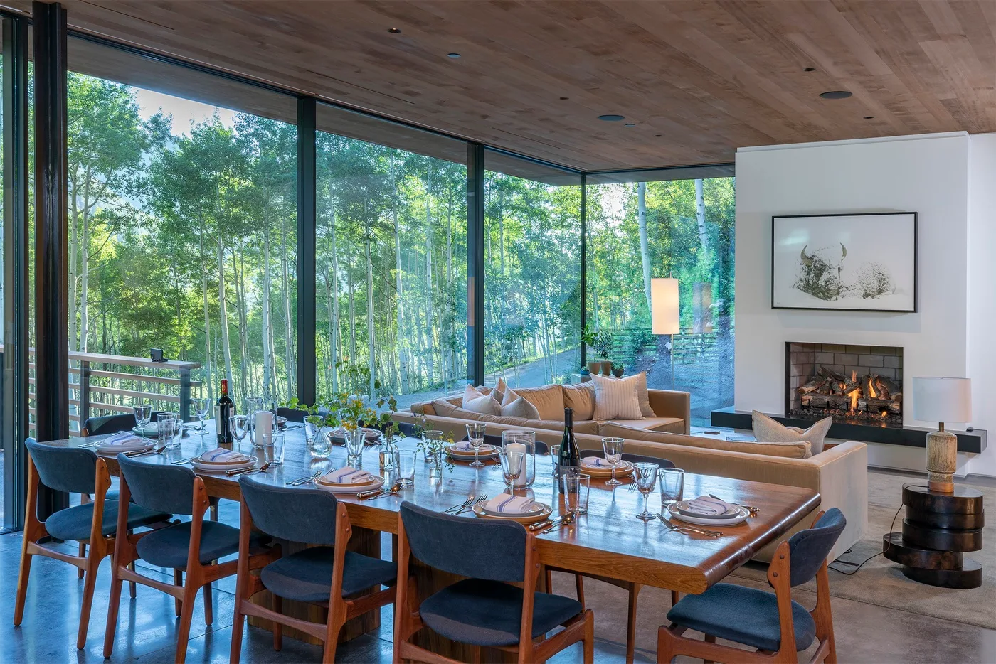 Un comedor y una zona de estar dan a un paisaje boscoso a través de ventanales.