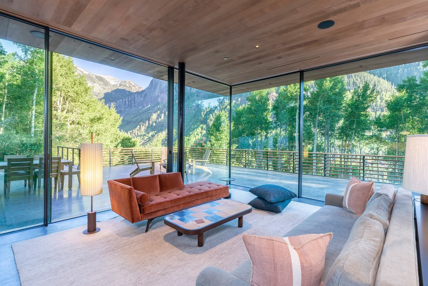 Una sala de estar moderna con asientos y ventanales que dan a árboles y montañas.