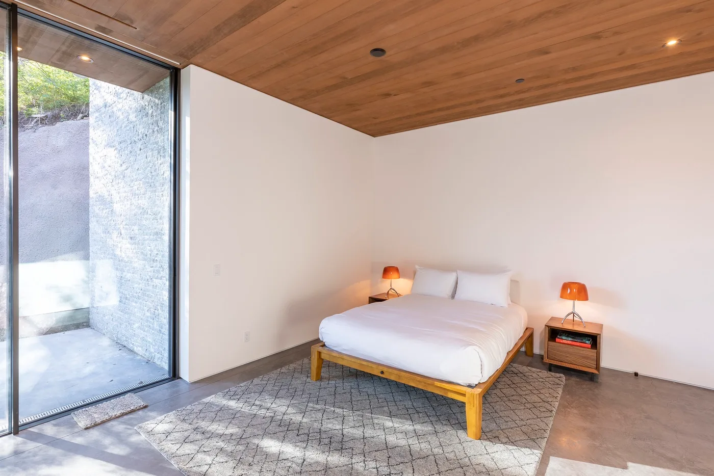 Un dormitorio con una cama junto a una gran ventana de vidrio.