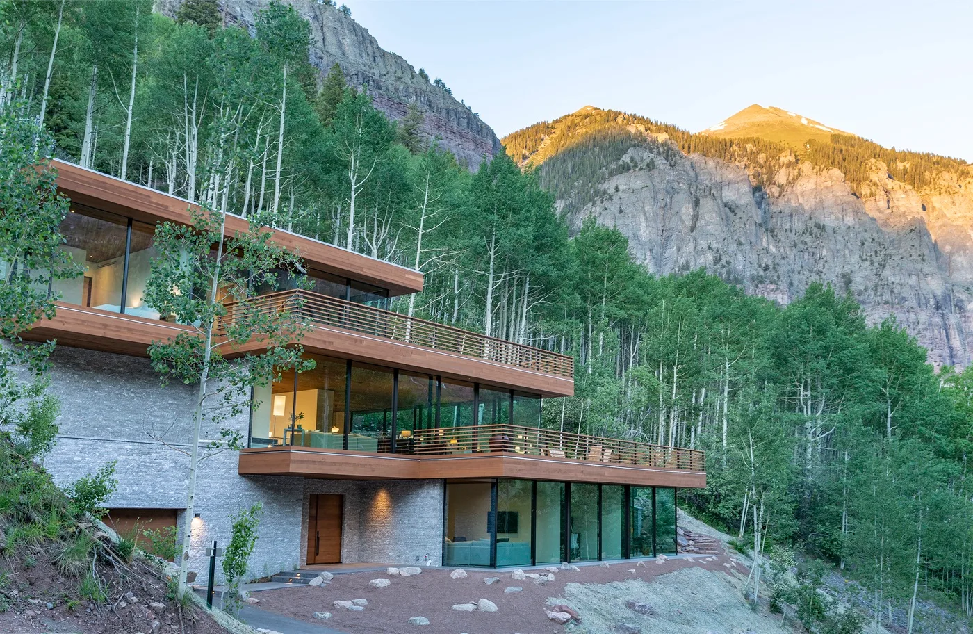 Una casa moderna se encuentra junto a una ladera montañosa boscosa.