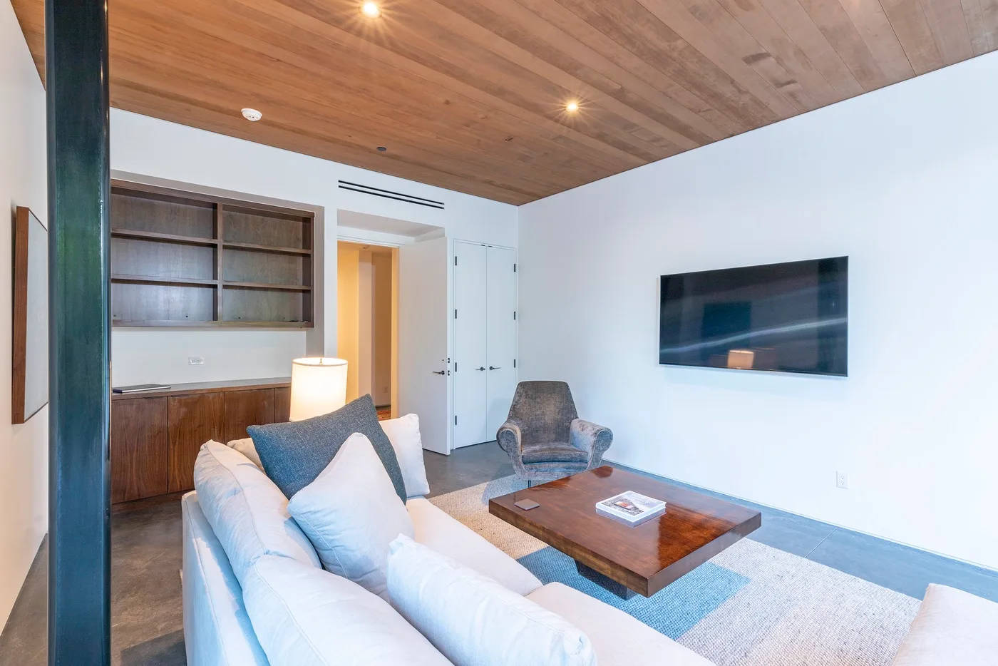 Una sala de estar con asientos, una mesa de centro de madera y un televisor en la pared.