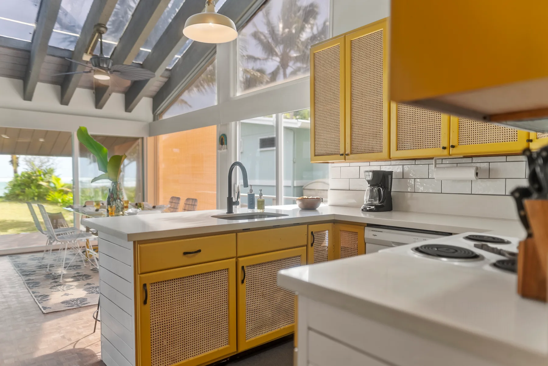 Una cocina luminosa con muebles amarillos, una isla central y grandes ventanas.
