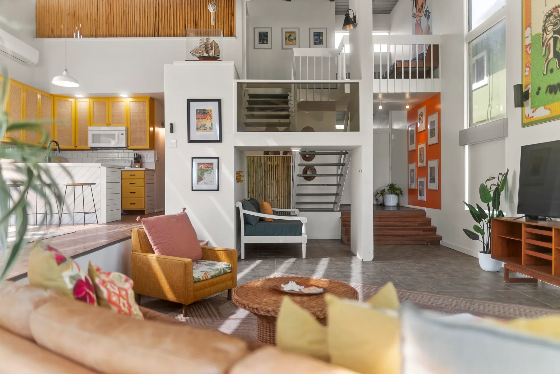 Una sala de estar diáfana con asientos de colores junto a una cocina y una escalera.