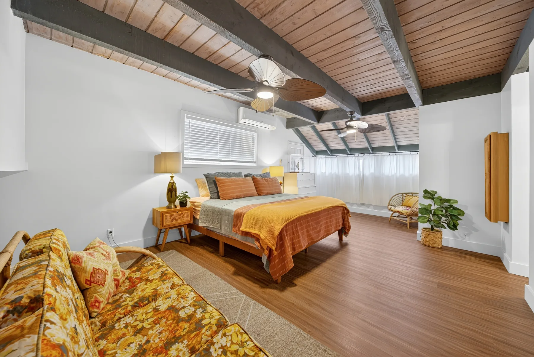 Un dormitorio con una cama, asientos estampados y un techo de madera inclinado.