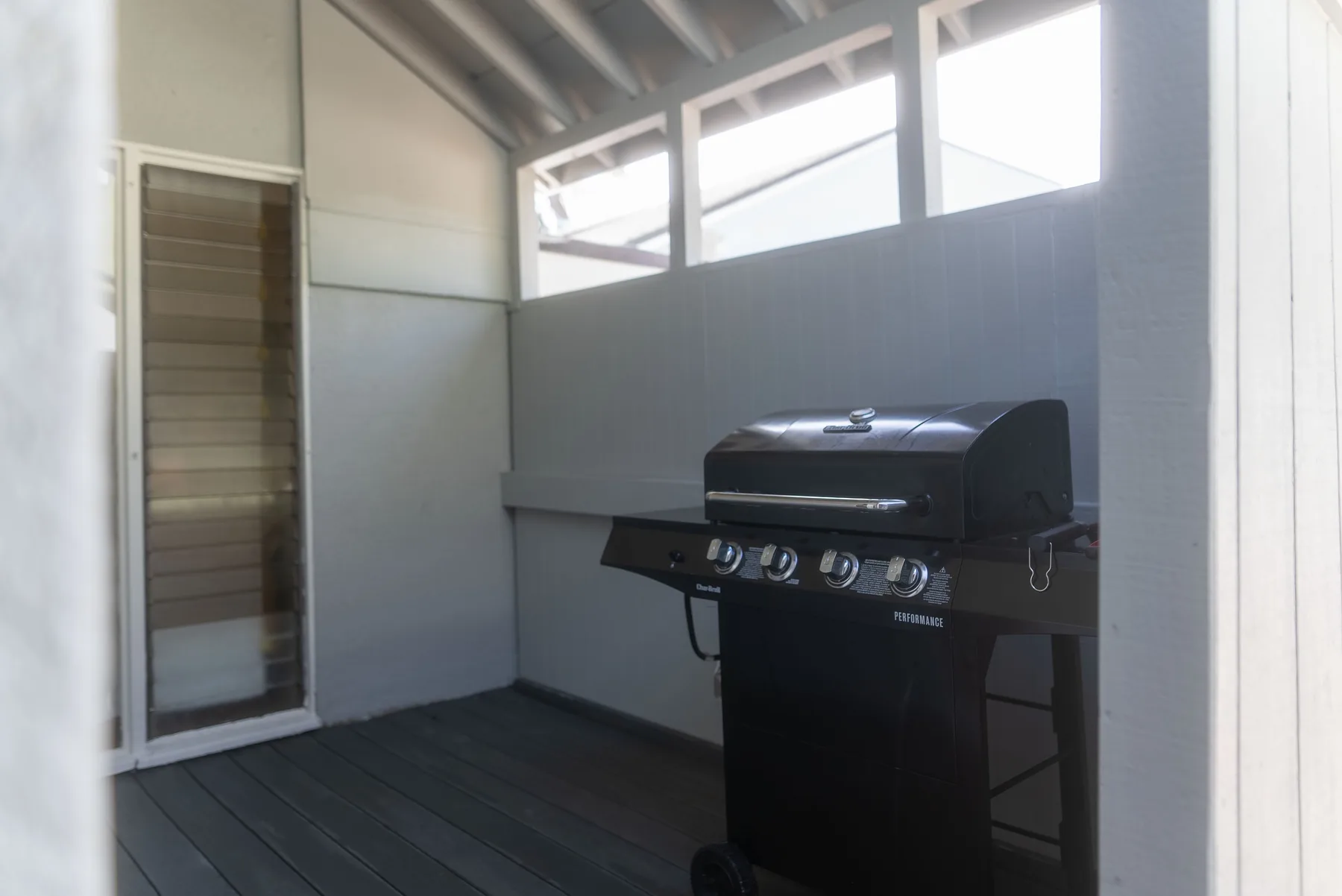 Una zona de cocina exterior cubierta con una parrilla junto a una puerta con mosquitera.