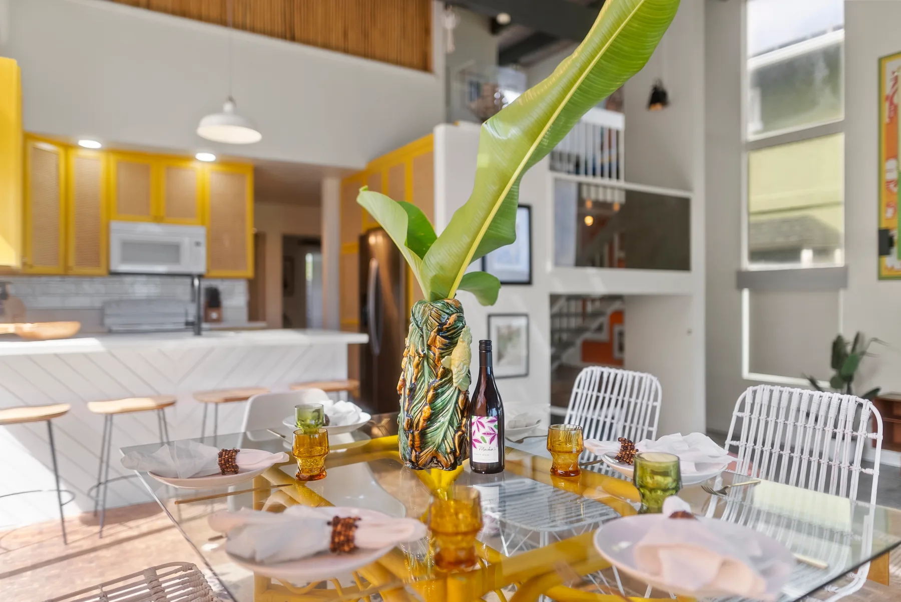 Comedor con una mesa de vidrio preparada con platos y bebidas de colores.