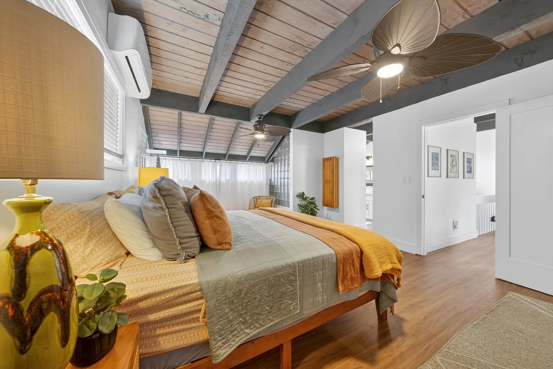 Un dormitorio con una cama, ropa de cama en tonos cálidos y vigas expuestas.