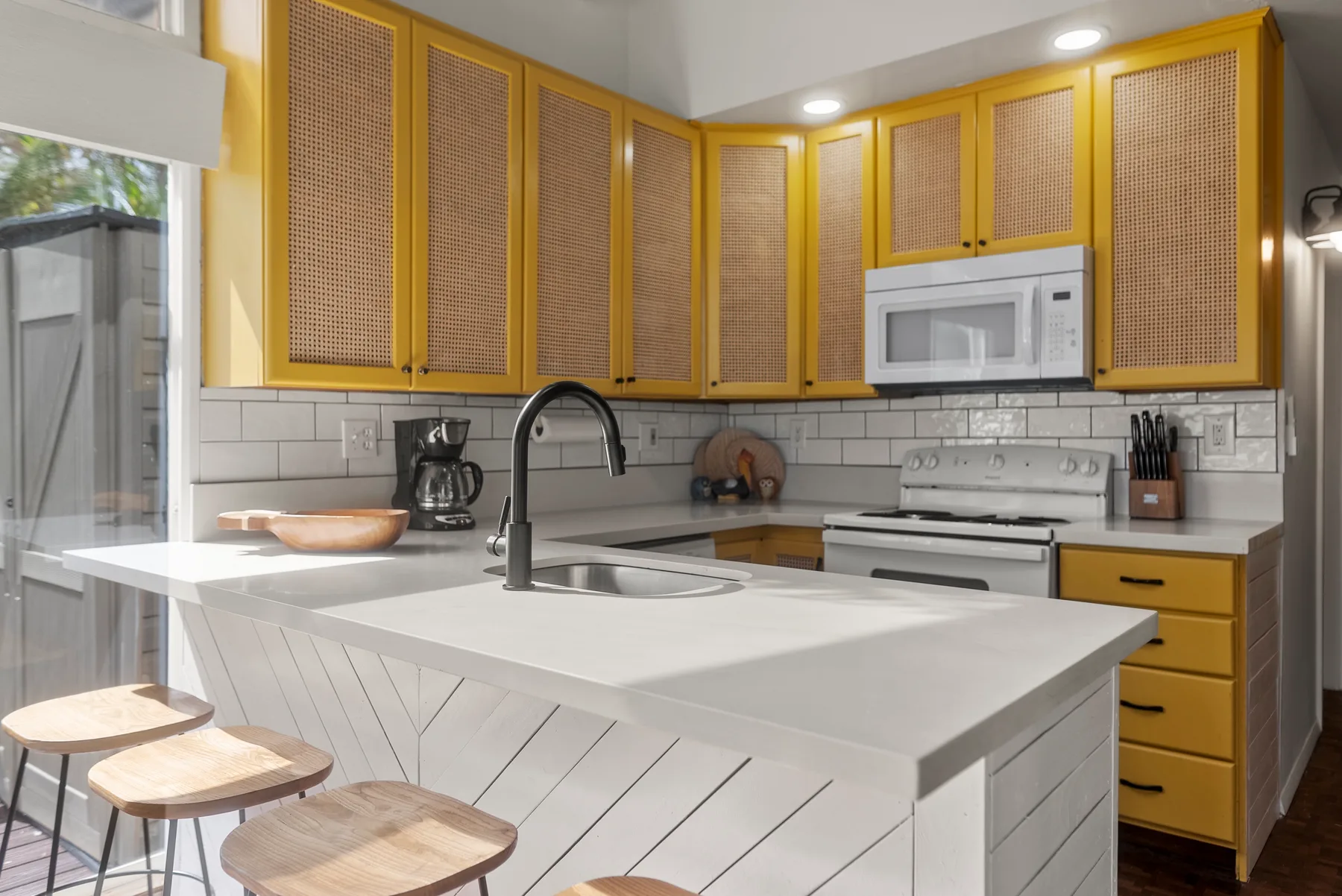 Una cocina luminosa con gabinetes amarillos, una isla blanca y bancos.