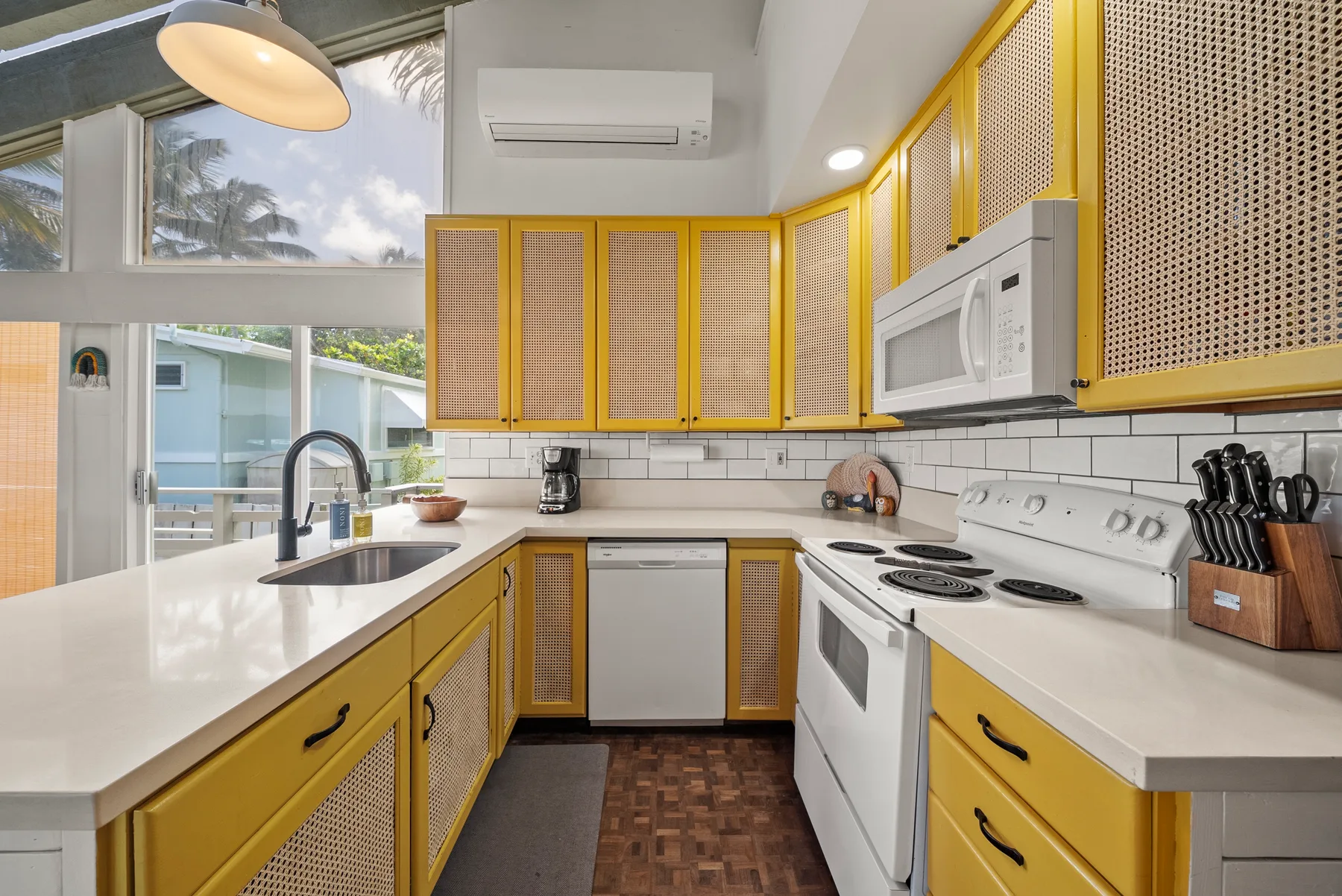 Una cocina luminosa con gabinetes amarillos, encimeras blancas y una ventana con vistas a la vegetación.
