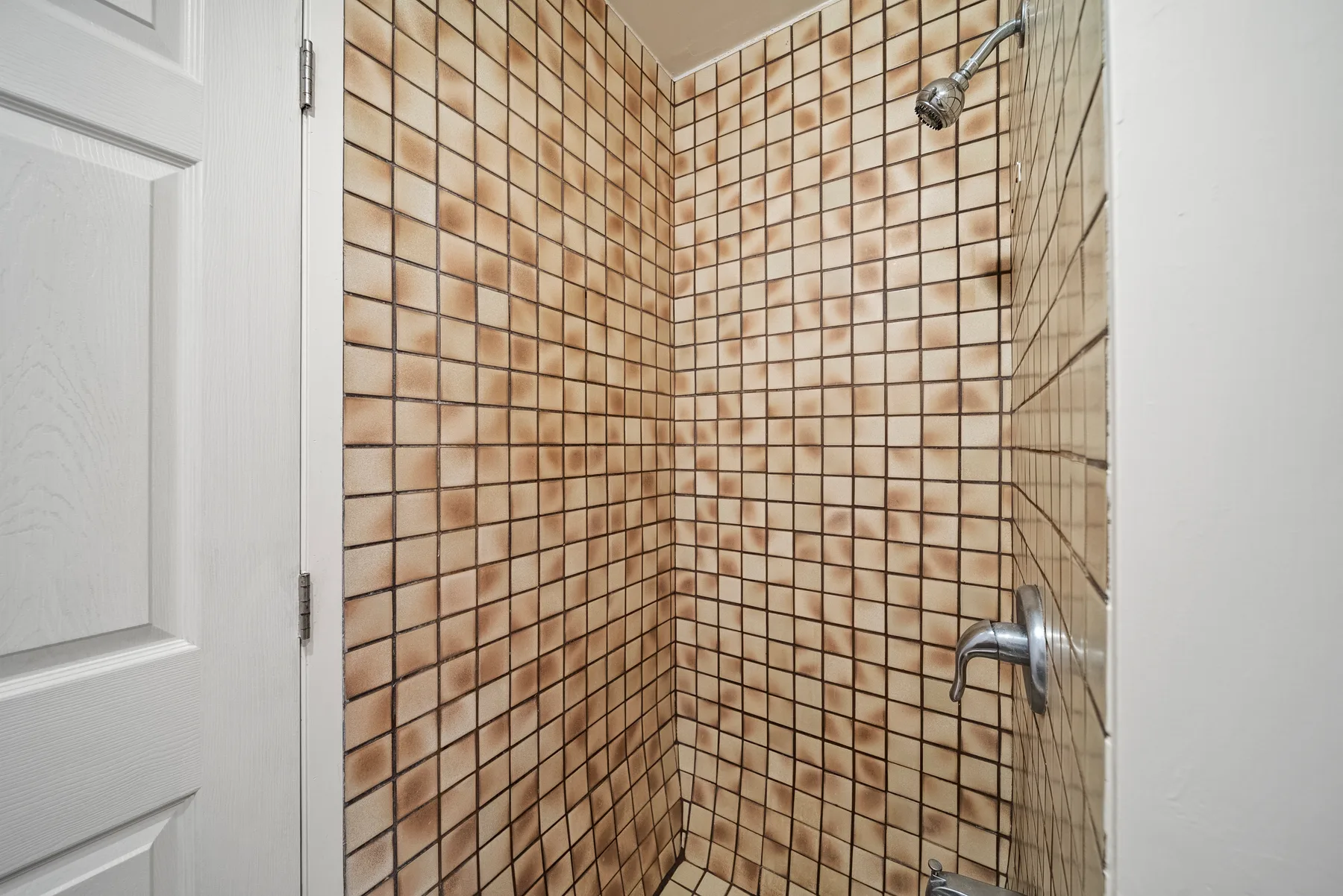 Una ducha con azulejos, rociador y controles.