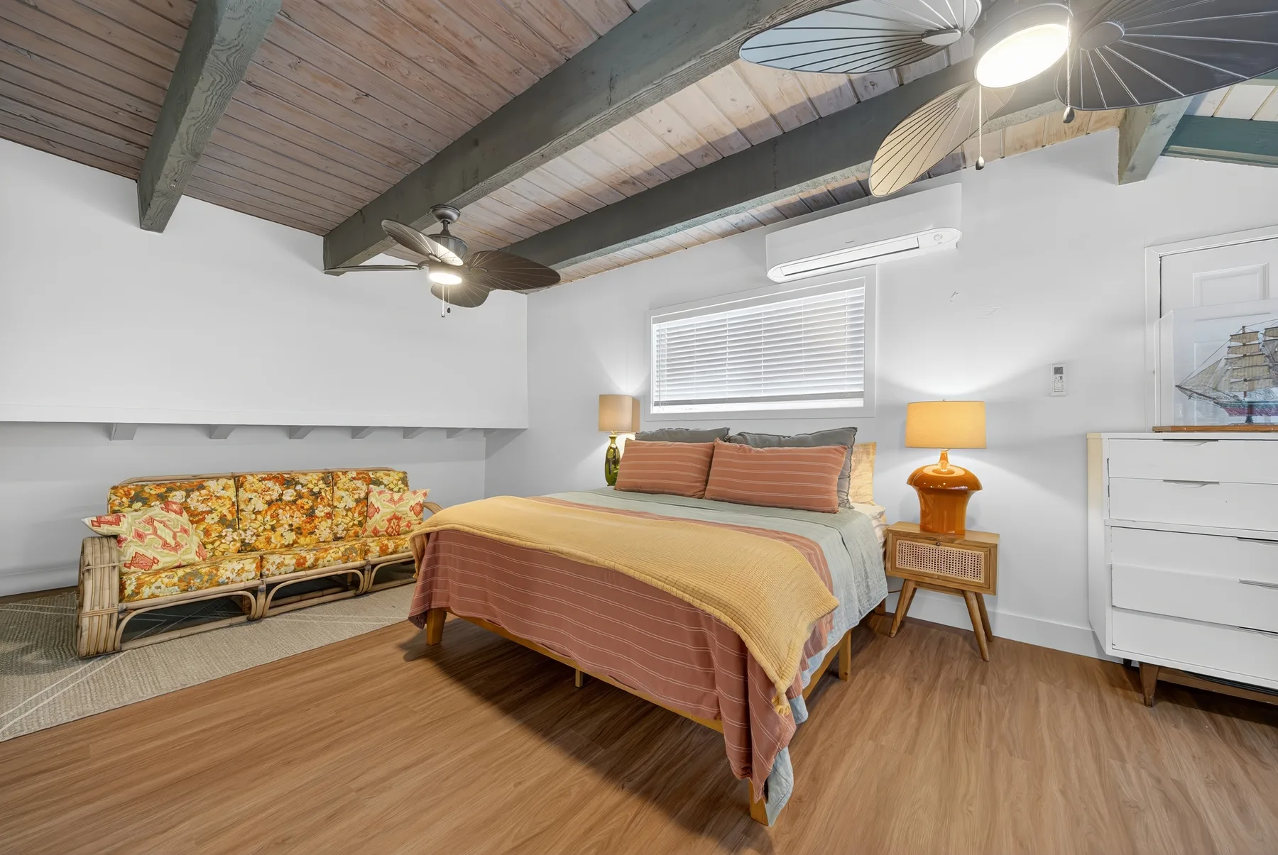 Un dormitorio con una cama, asientos estampados y una ventana con persianas.