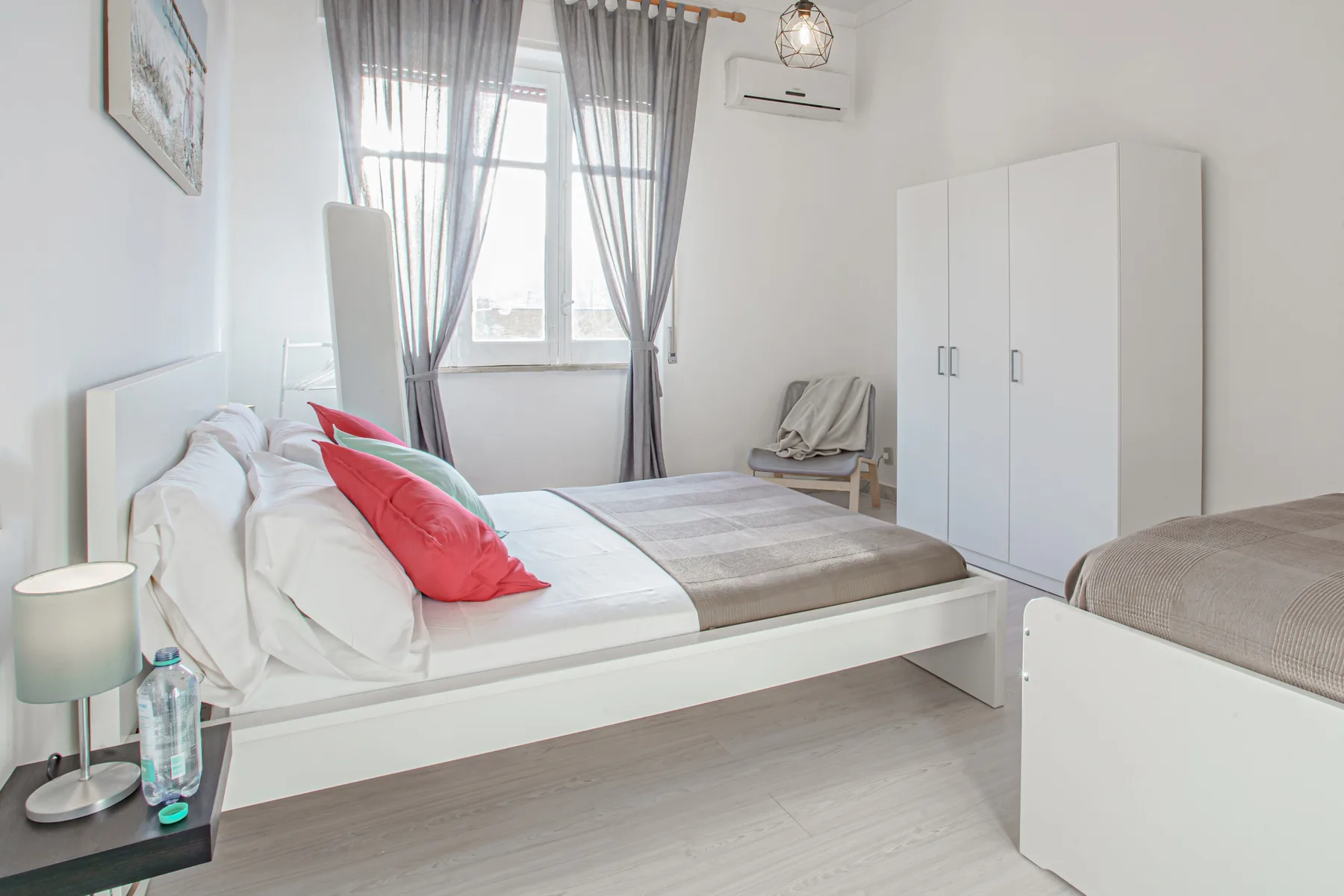 A bright bedroom with a bed, wardrobe, and curtained window.