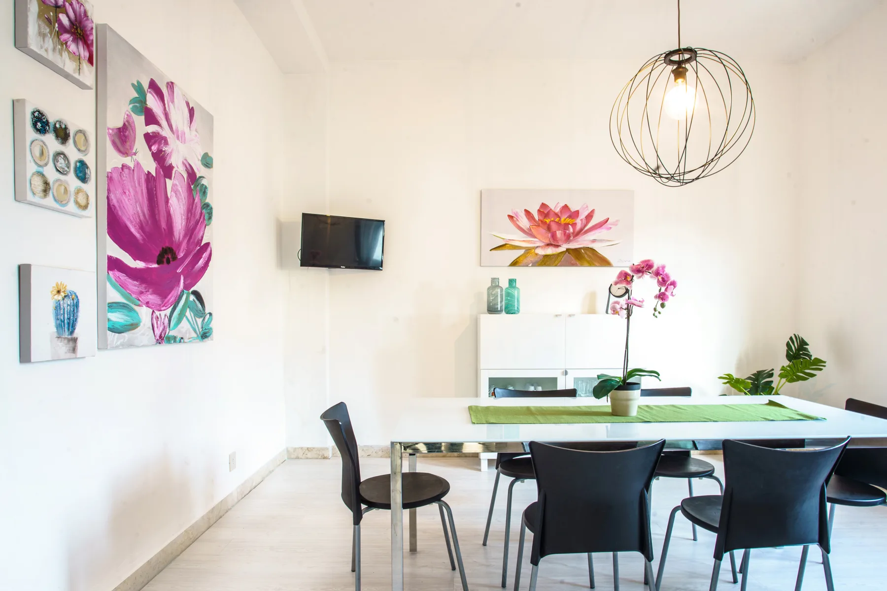 A bright dining area with a table, chairs, and colorful floral artwork.
