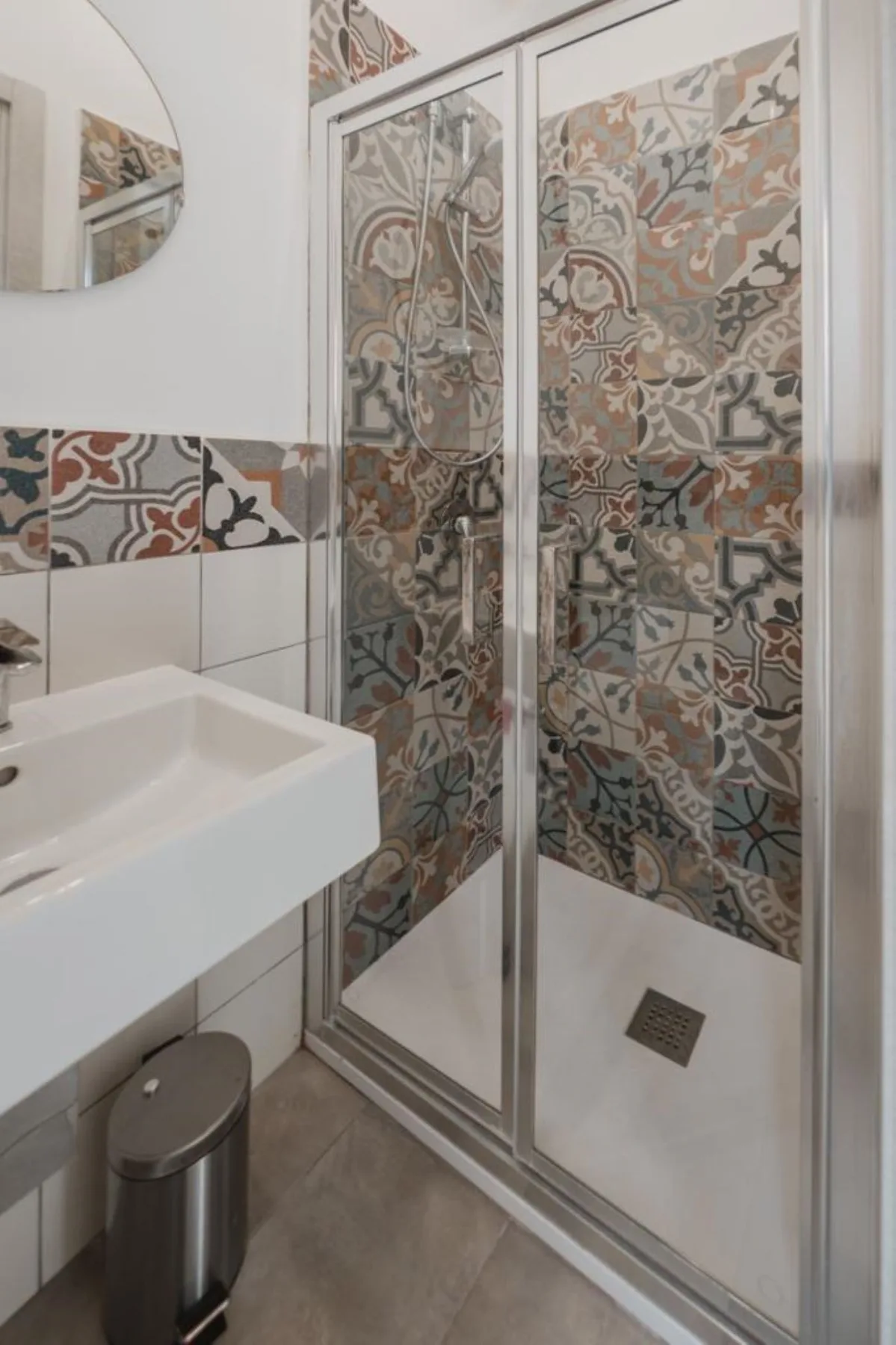 A bathroom with a glass-enclosed shower and patterned wall tiles.