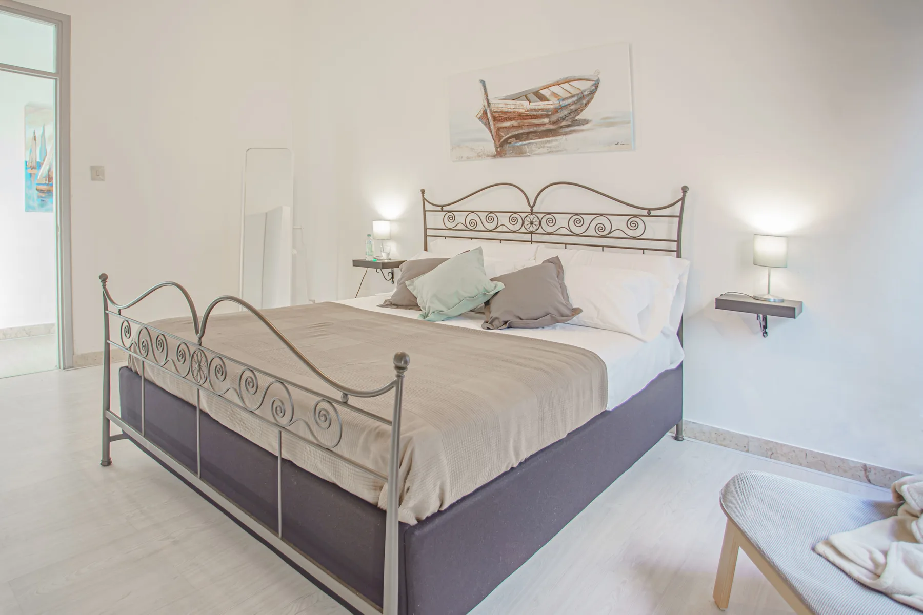 A bedroom with a metal bed, neutral bedding, and a boat picture above the headboard.