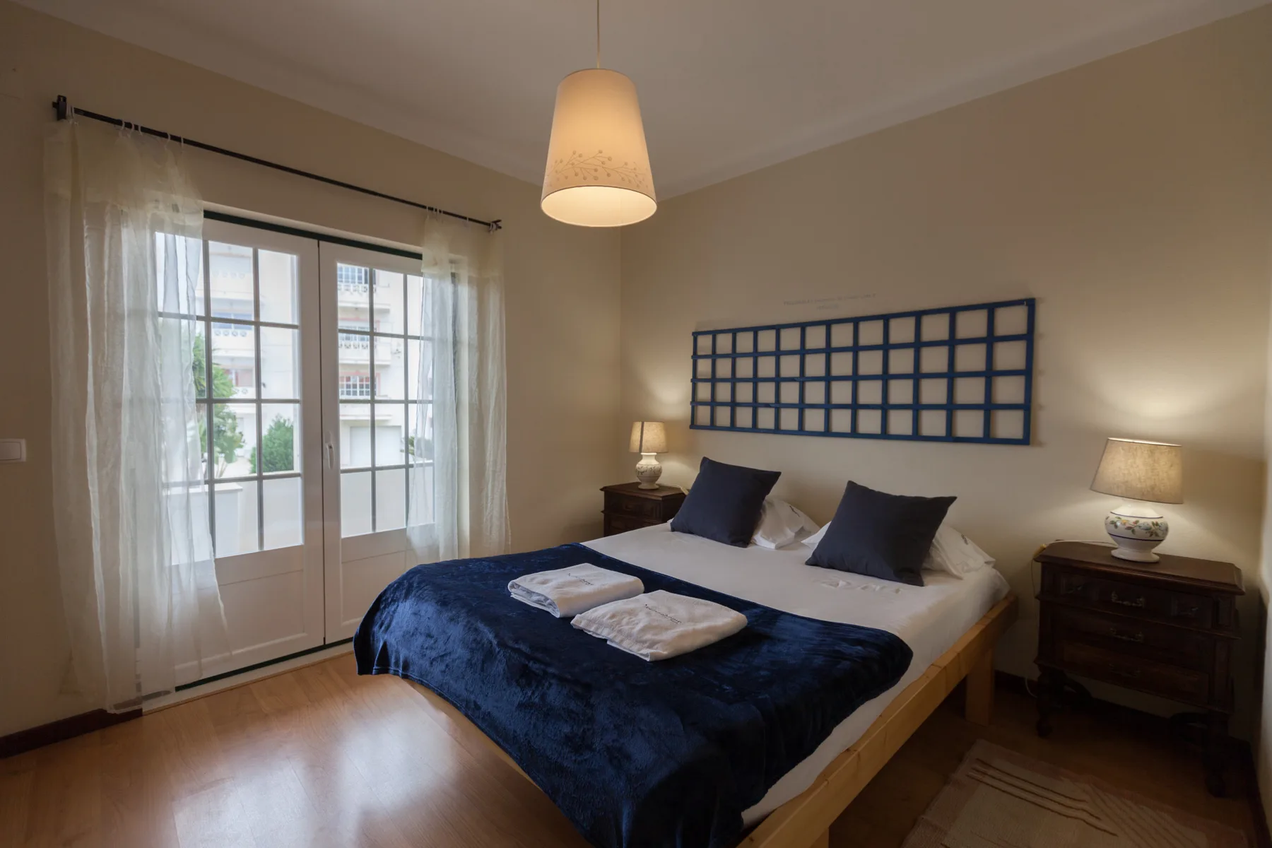 A bedroom with a bed dressed in dark blue bedding and large windows.