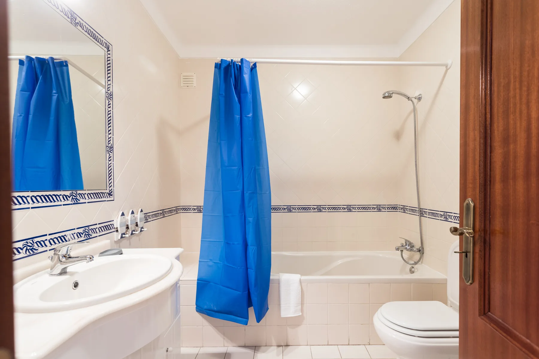 A tiled bathroom with a sink, bathtub, toilet, and blue shower curtain.