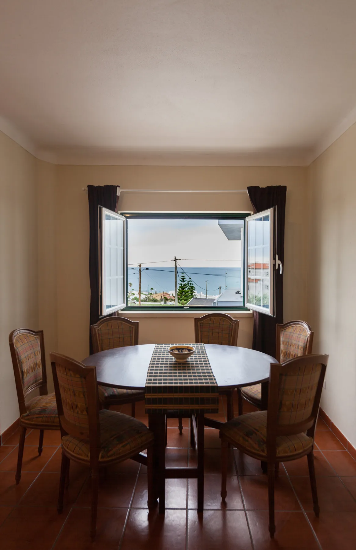 A dining room with a round table and open windows overlooking the town.