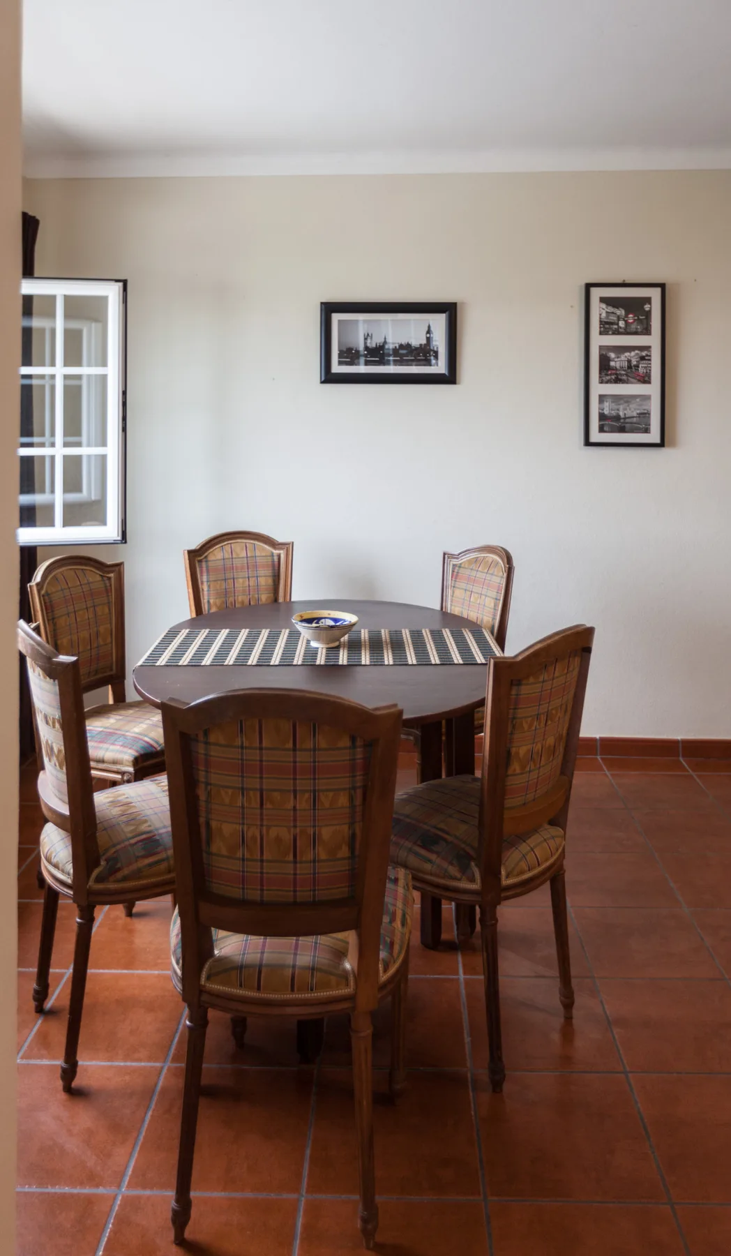 A dining area with a rectangular table, chairs, and framed pictures on the wall.