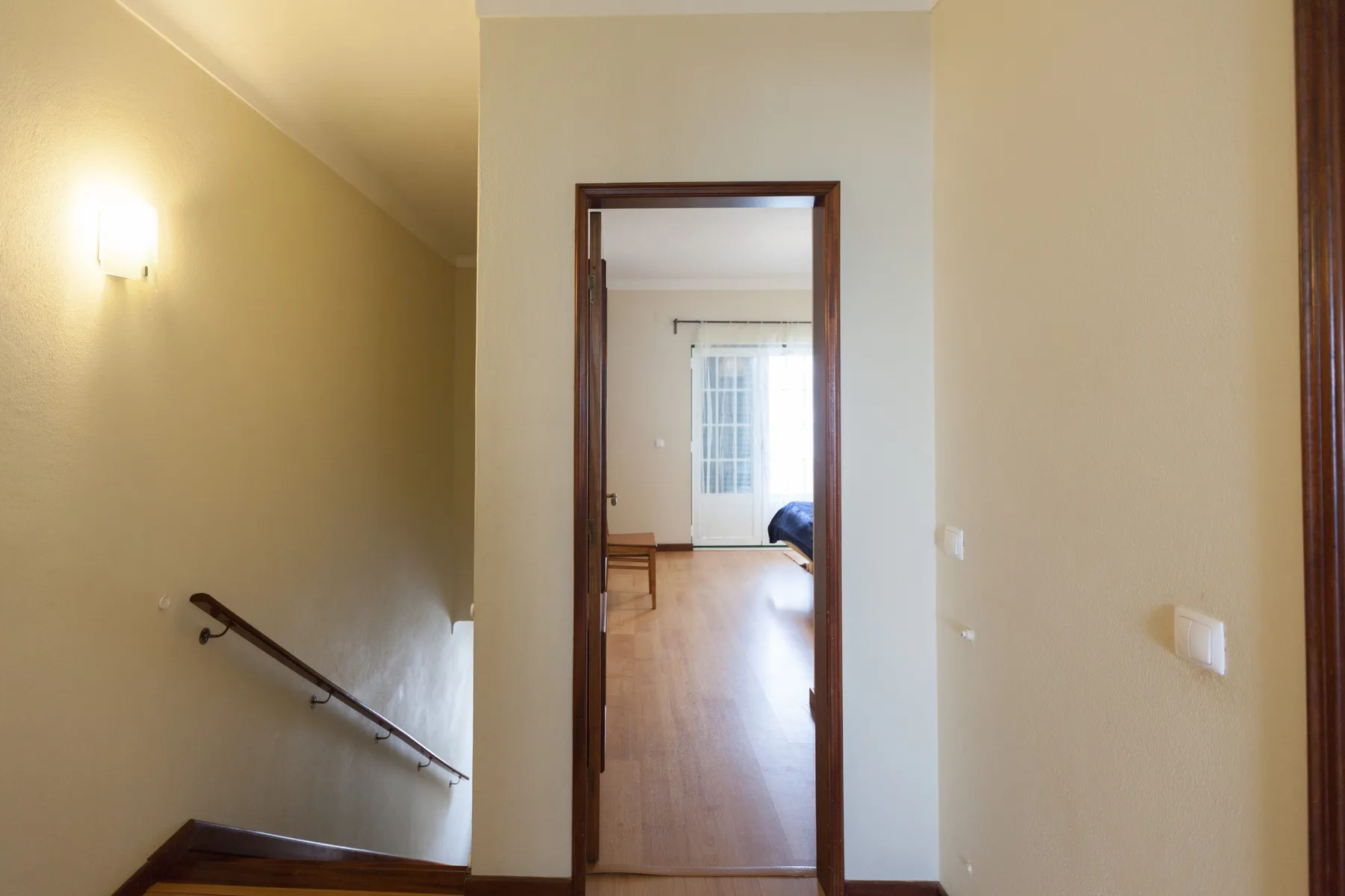 A hallway opens onto a bright room with a window and wood flooring.