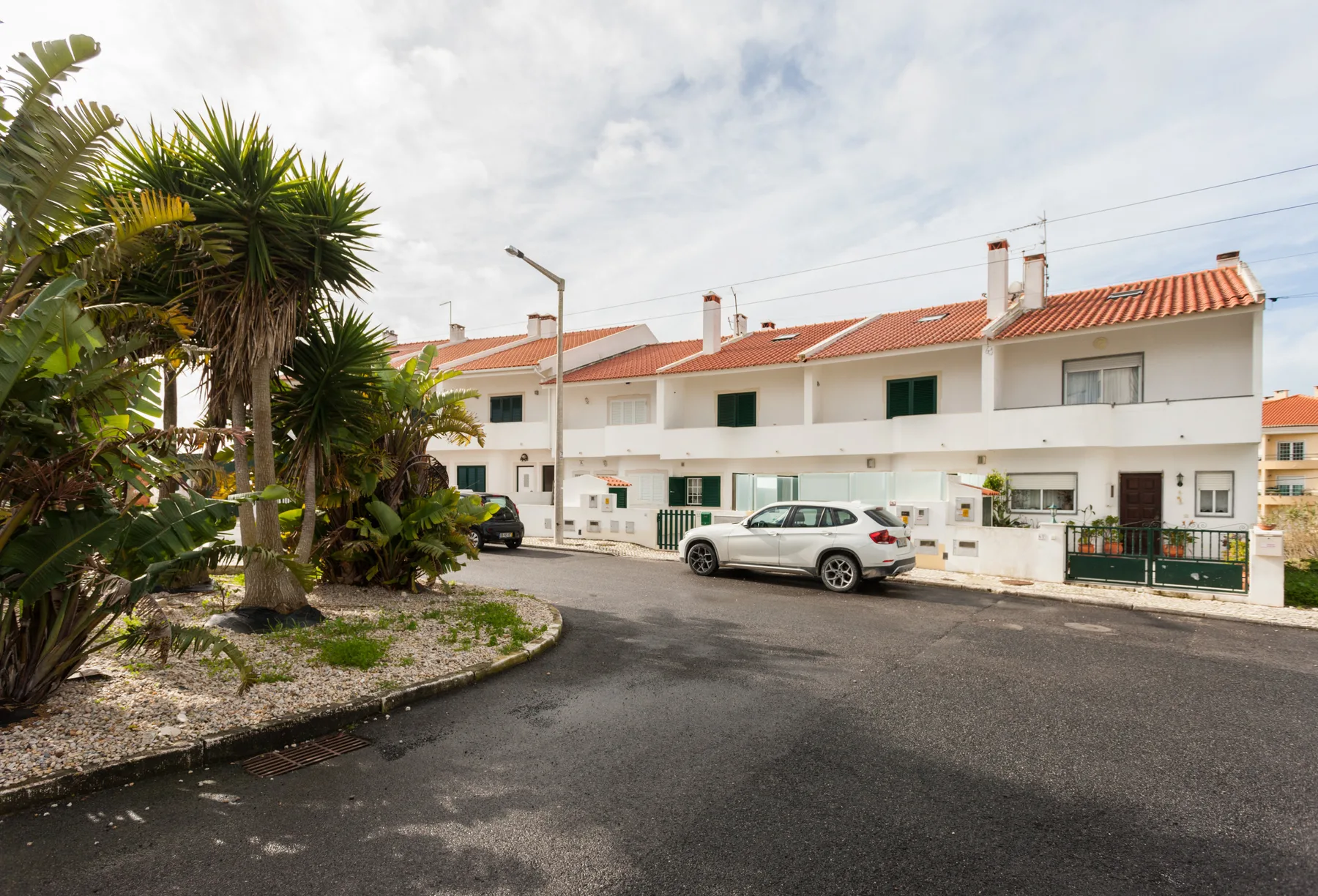 A row of white homes with red roofs faces a paved street.