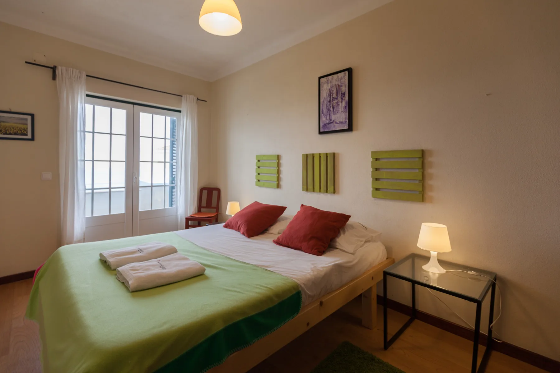 Dormitorio con cama doble, colcha verde y ventanas luminosas.