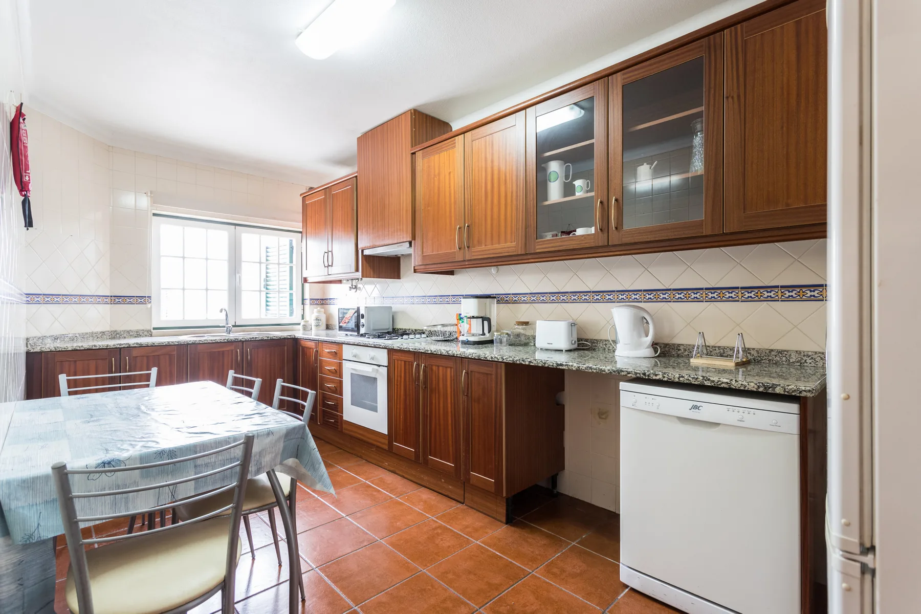 A tiled kitchen with wooden cabinets, countertop appliances, and a dining table.