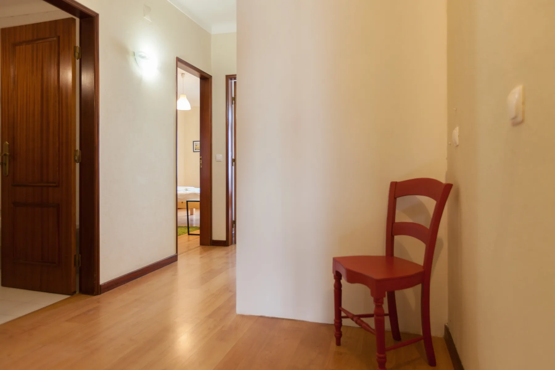 A hallway with a red chair beside an open doorway.