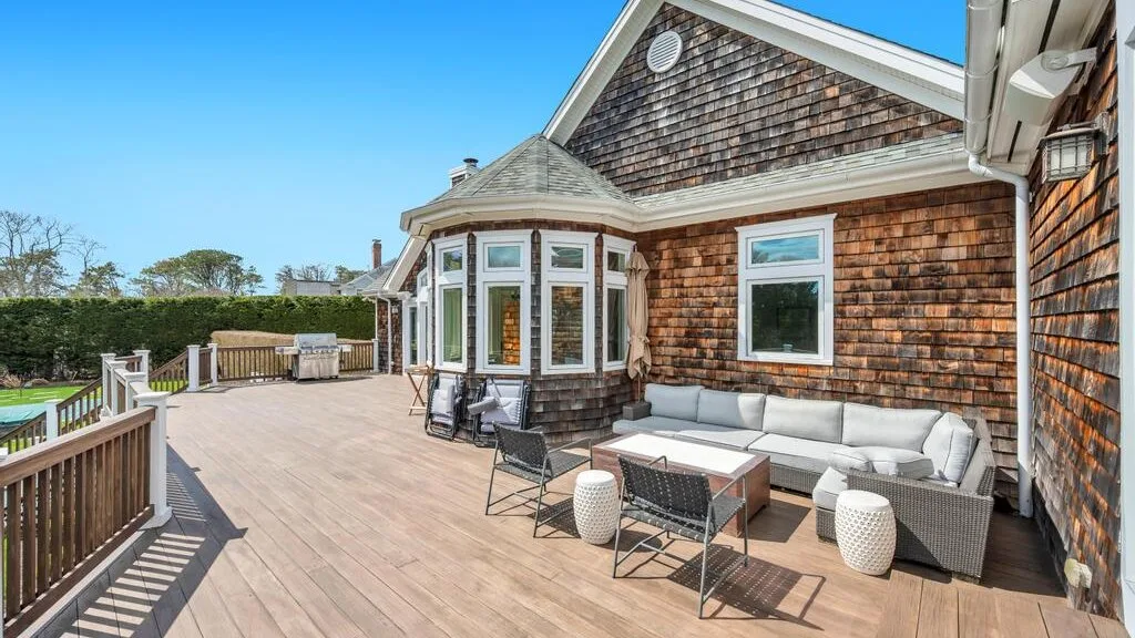 A spacious outdoor deck beside a shingle-sided house, with seating and a dining table.