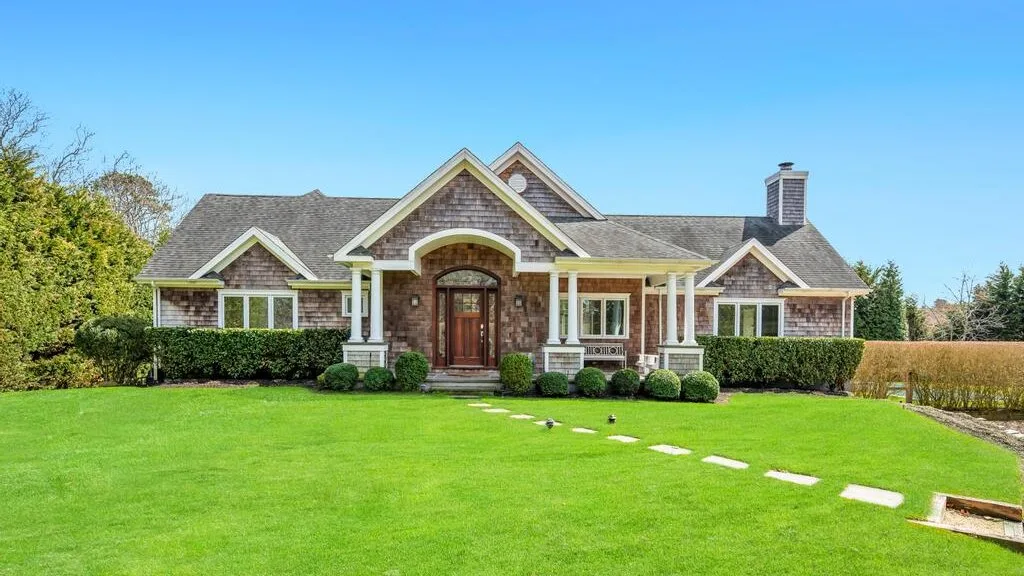 A large house stands behind a broad green lawn under a clear blue sky.
