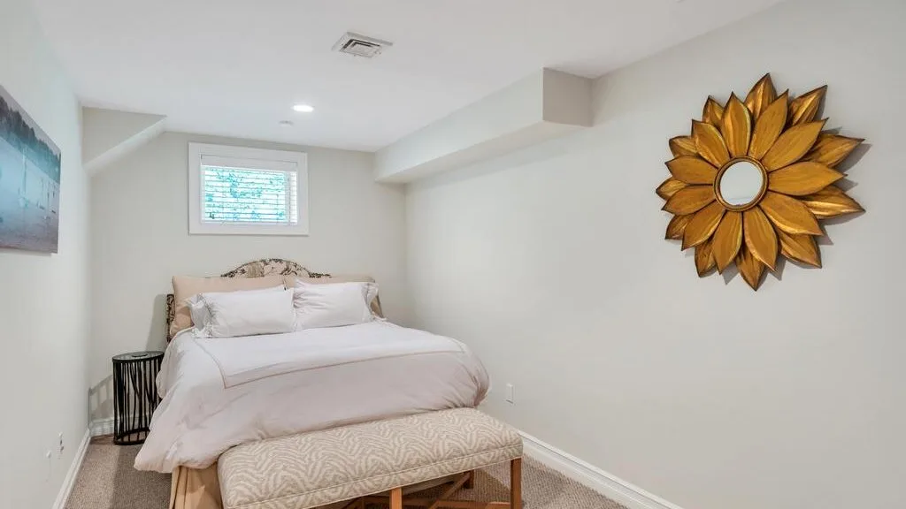 A bedroom with a neatly made bed and a decorative sunburst mirror.