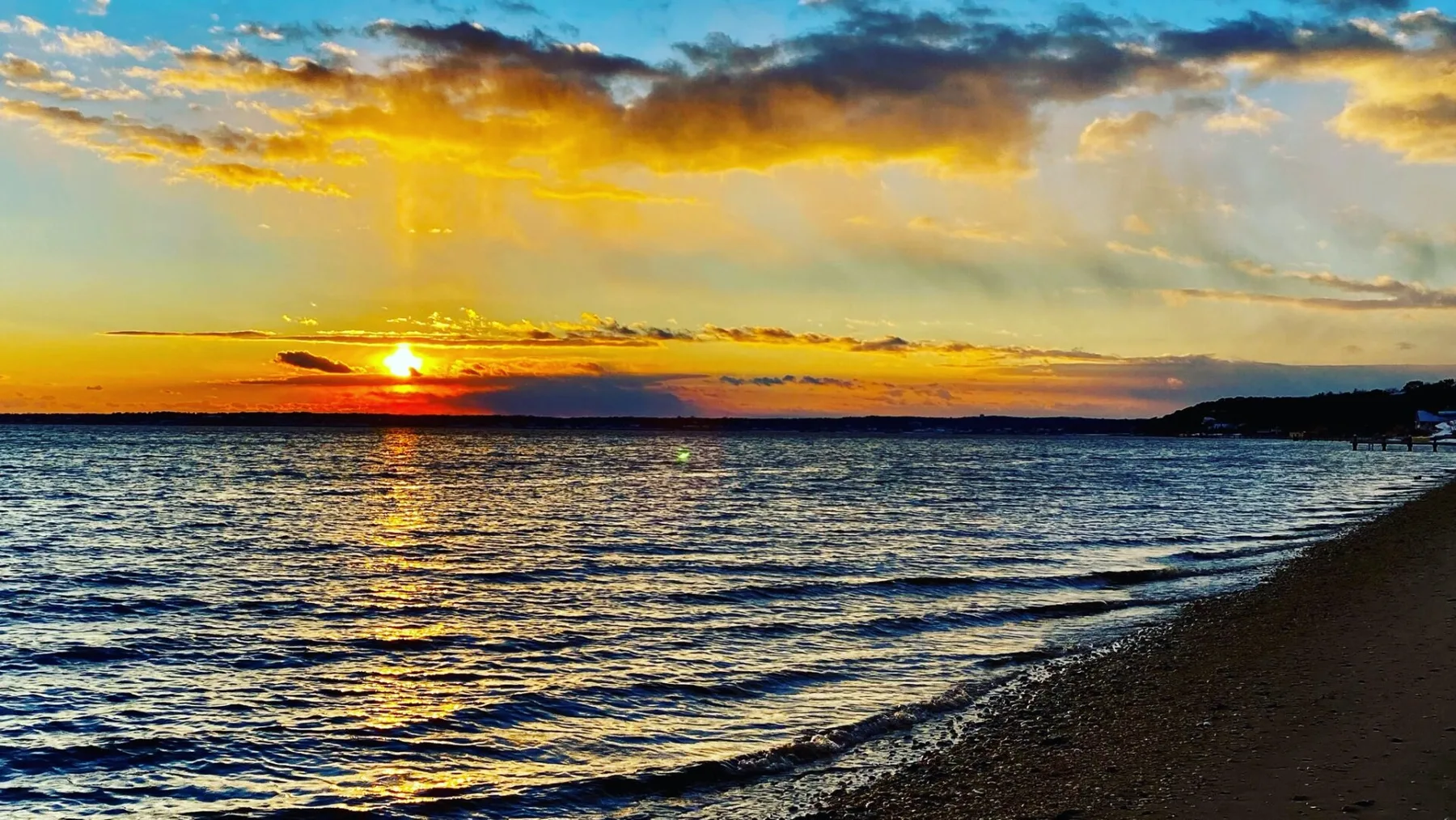 A sunset glows over the water beside a dark shoreline.