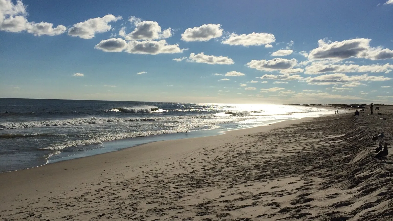 A sandy beach meets the ocean beneath a partly cloudy sky.