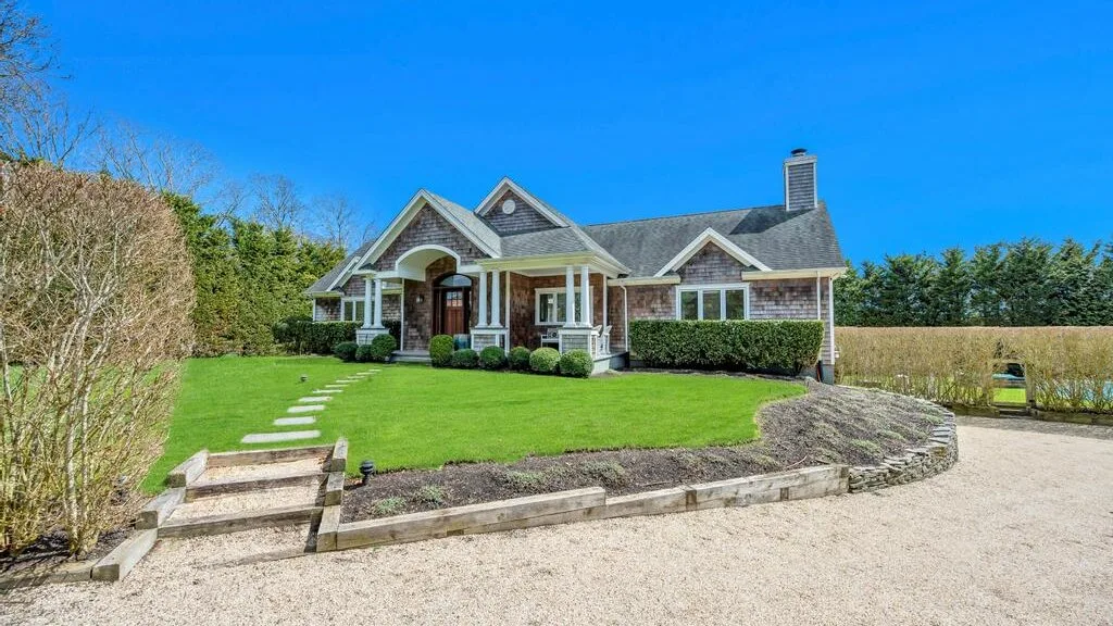 A house stands beside a green lawn and a gravel driveway.