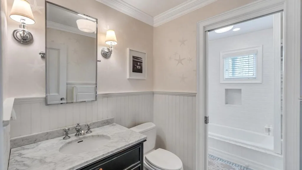 A bathroom with a marble-patterned vanity, mirror, and toilet.