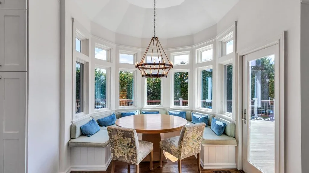 A bright dining nook has a round table, chairs, and curved window seating.