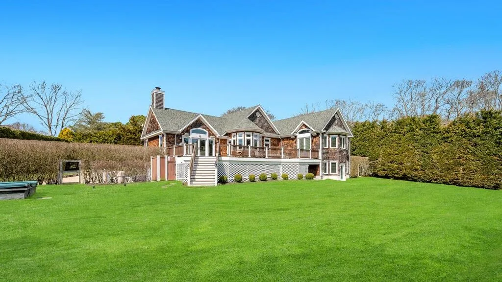 A large house stands beyond a broad green lawn under a clear blue sky.