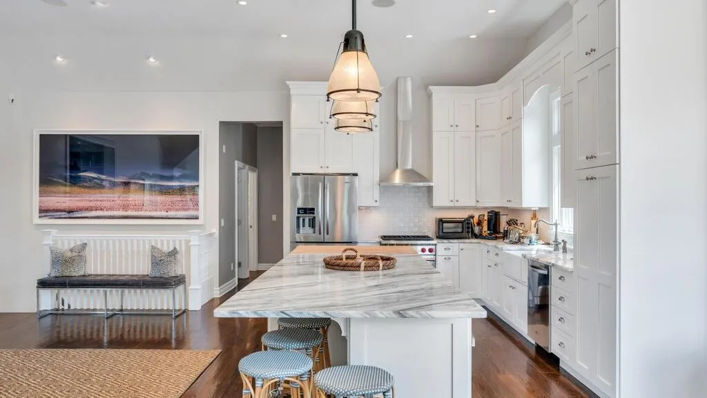 A bright kitchen with white cabinetry, a marble island, and bar seating.