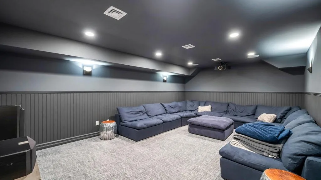 A basement-style lounge with blue seating arranged around a central ottoman.