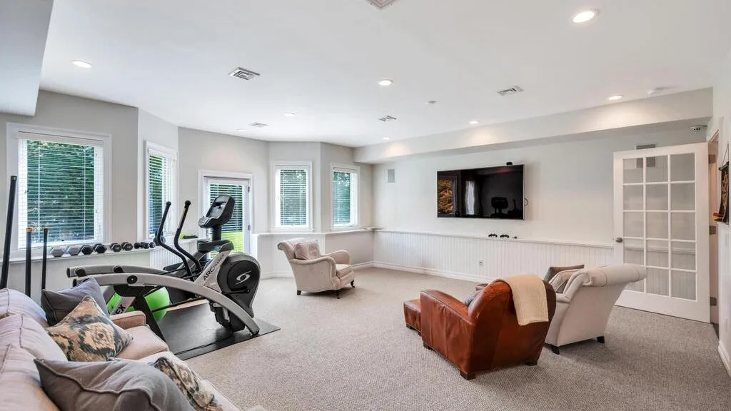 A bright living room with exercise equipment and seating around a wall-mounted television.