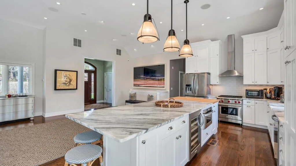 A bright kitchen with a large island, pendant lights, and stainless steel appliances.