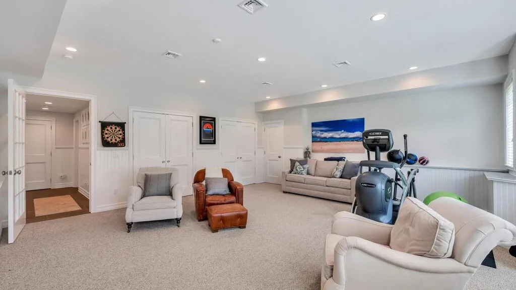 A bright basement recreation room with seating and exercise equipment.
