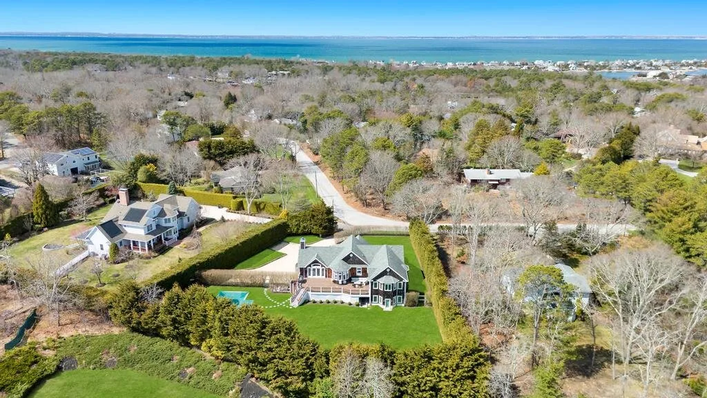 An aerial view shows houses among trees, with the coastline visible in the distance.