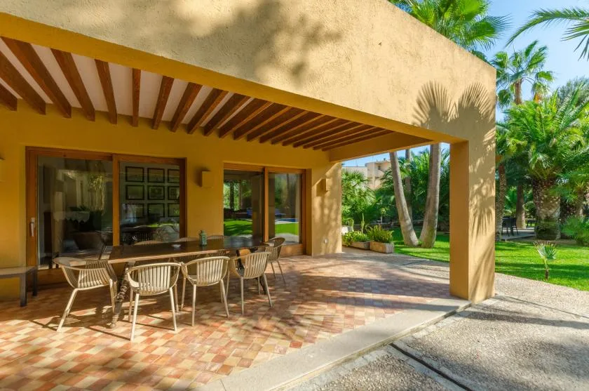Un patio cubierto con asientos al aire libre da a un jardín verde.