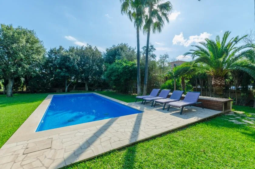 Una piscina al aire libre está rodeada por una terraza pavimentada, asientos y césped verde.