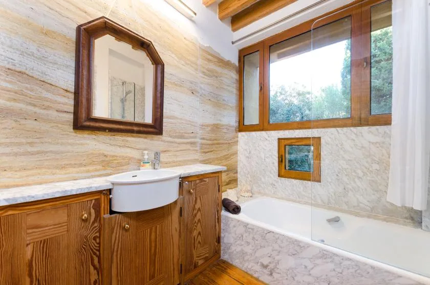 Un baño con bañera, lavabo y una ventana sobre la bañera.