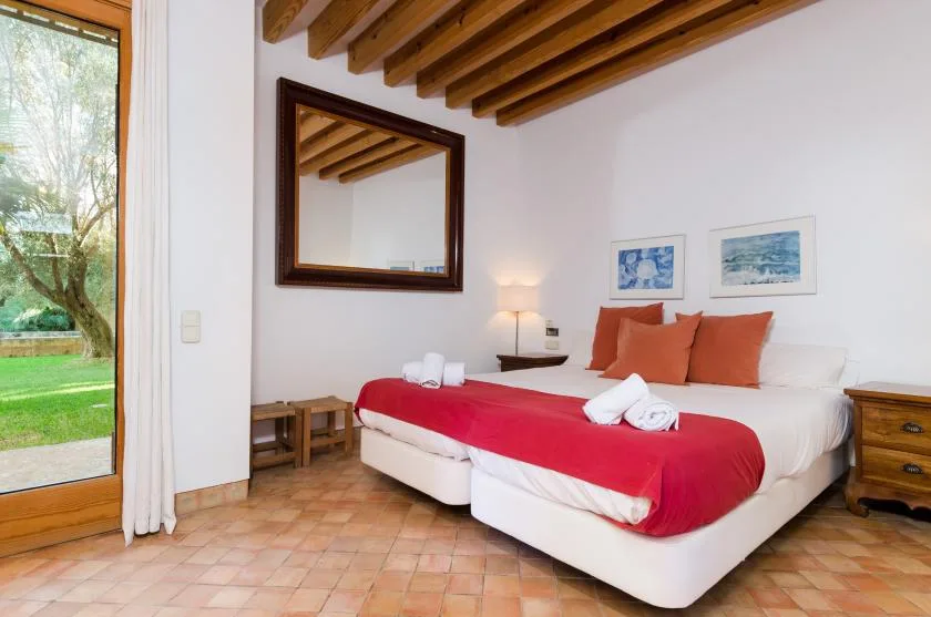 Un dormitorio con una cama vestida de rojo y una puerta de cristal con vistas a un jardín.